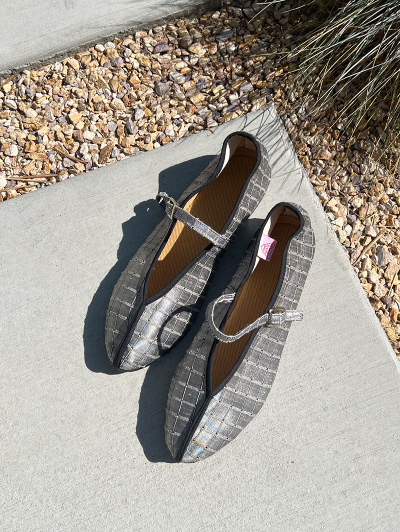 Pair of gray flats with a strap on a concrete surface.